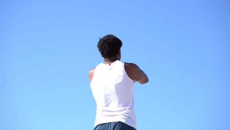 Back-view-of-man-stretching-arms-against-blue-sky